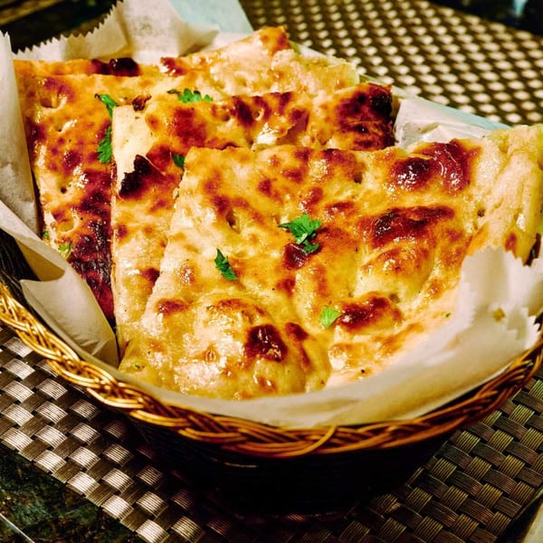 Golden brown naan bread, garnished with herbs, served in a woven basket at CURRY ZONE.