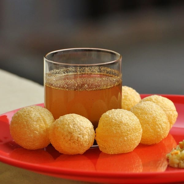 Pani Puri, a popular Indian street food, with a glass of spiced water and crispy hollow balls.