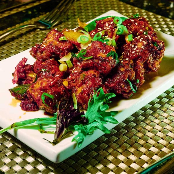 CURRY ZONE's vibrant red Indian dish, garnished with sesame seeds and green onions, on a white plate.