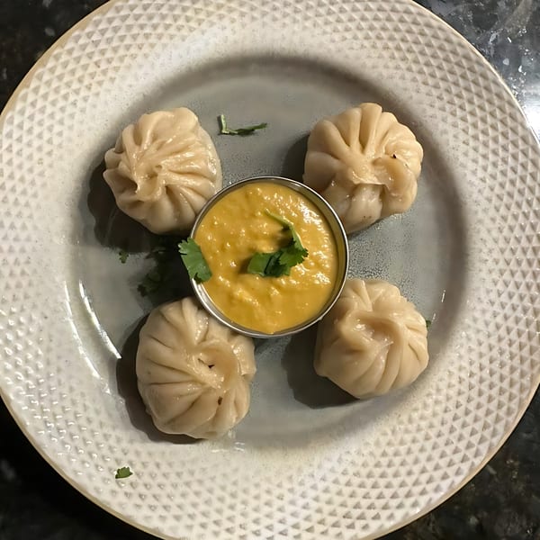 Four steamed momos arranged around a small bowl of yellow dipping sauce, garnished with cilantro.