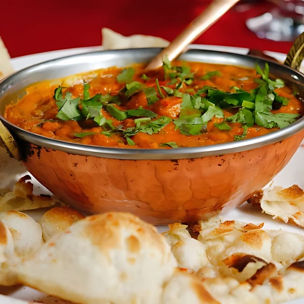 A copper bowl of Indian curry, garnished with cilantro, served with naan bread.