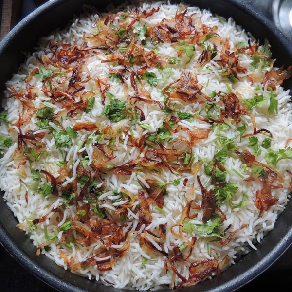 Close-up of Indian biryani rice topped with crispy fried onions and fresh cilantro in a black pot.