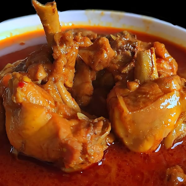 Close-up of Indian chicken curry with rich red sauce and tender chicken pieces in a white bowl.