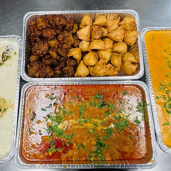 CURRY ZONE Indian catering spread with samosas, pakoras, butter chicken, and rice in foil trays.