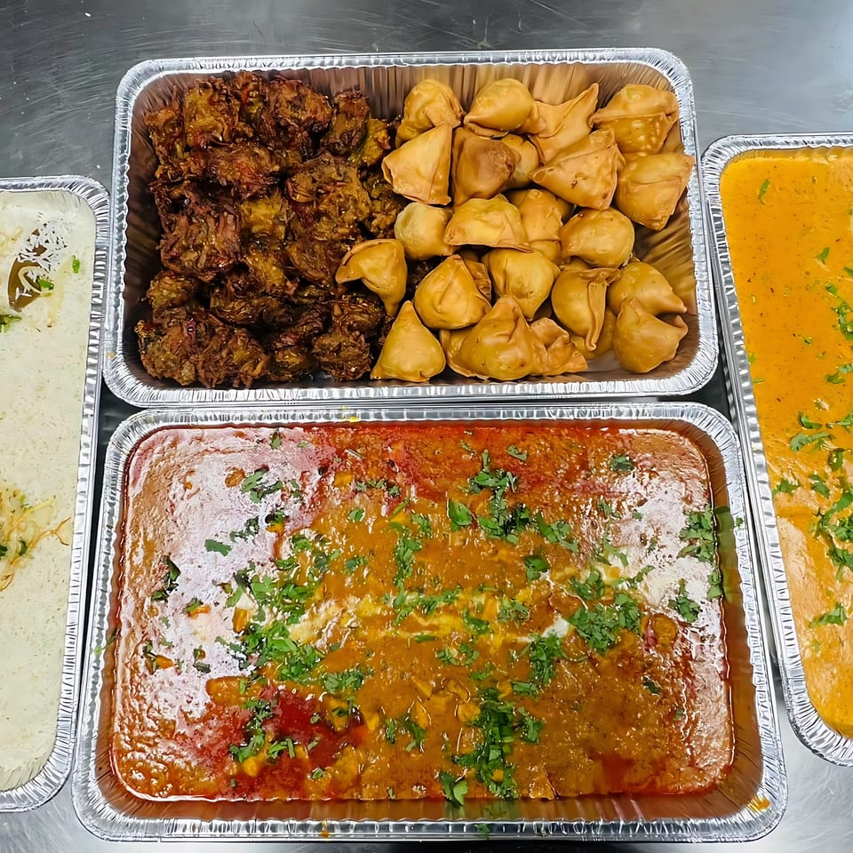 CURRY ZONE Indian catering spread with samosas, pakoras, butter chicken, and rice in foil trays.