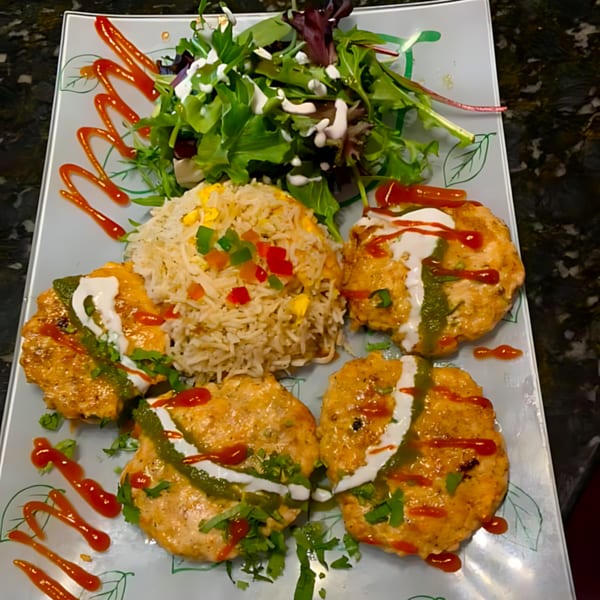 Indian dish with four chicken patties, rice, and a side salad, garnished with sauces and herbs.