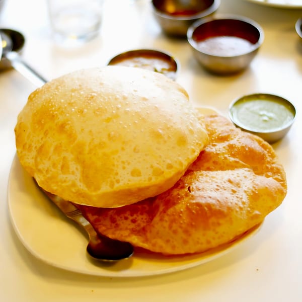 Golden-brown Indian puri bread on a white plate with small bowls of sauces.